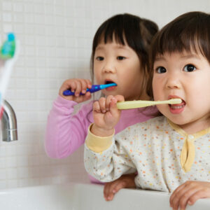 Two girl toddlers brushing teeth at bathroom sink