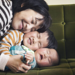 Japanese older brother embraces his younger sister, while their mother joins in on the sofa.