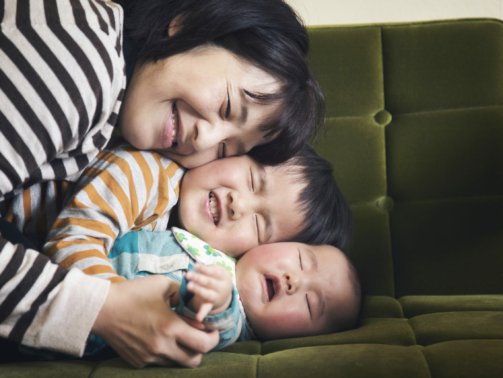 Japanese older brother embraces his younger sister, while their mother joins in on the sofa.