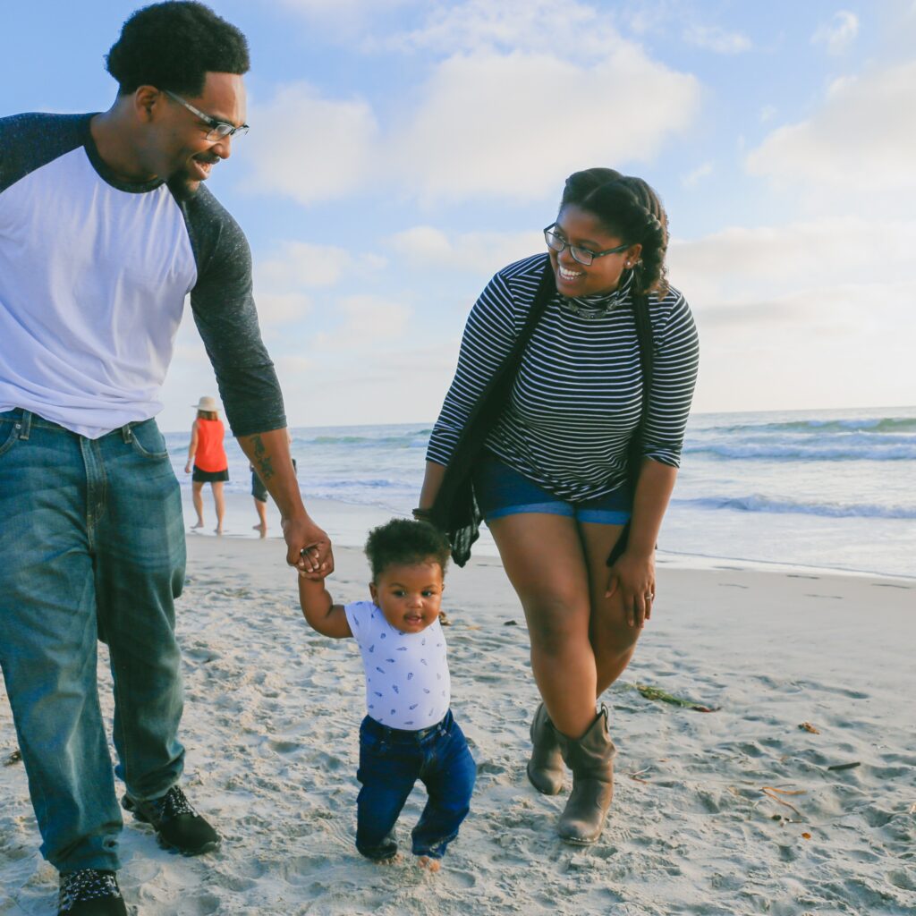A black couple walking on the beach with their baby.