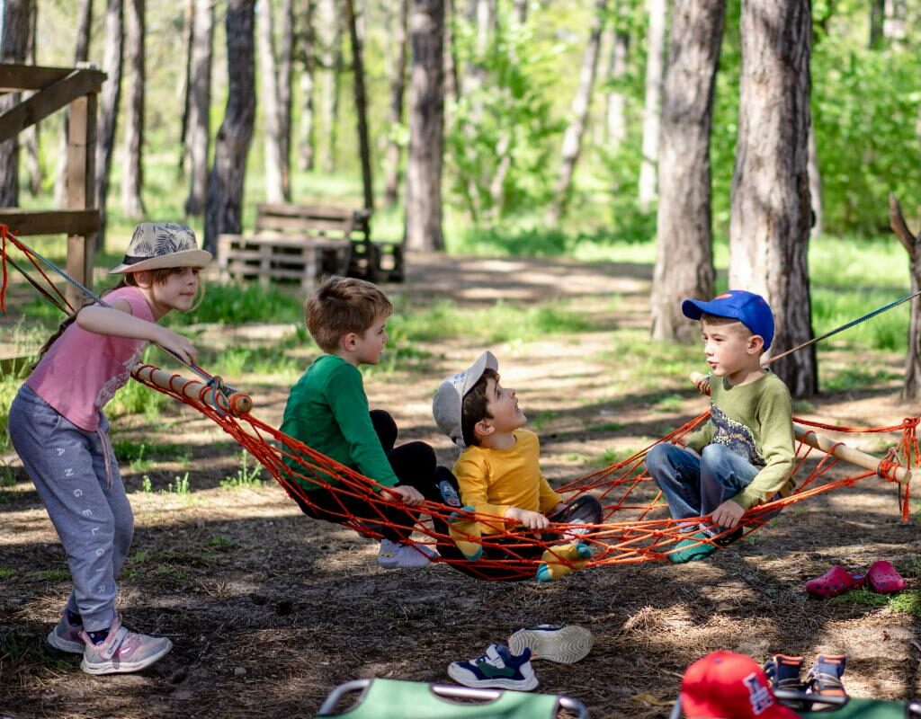 Three young children play on a hammock among trees