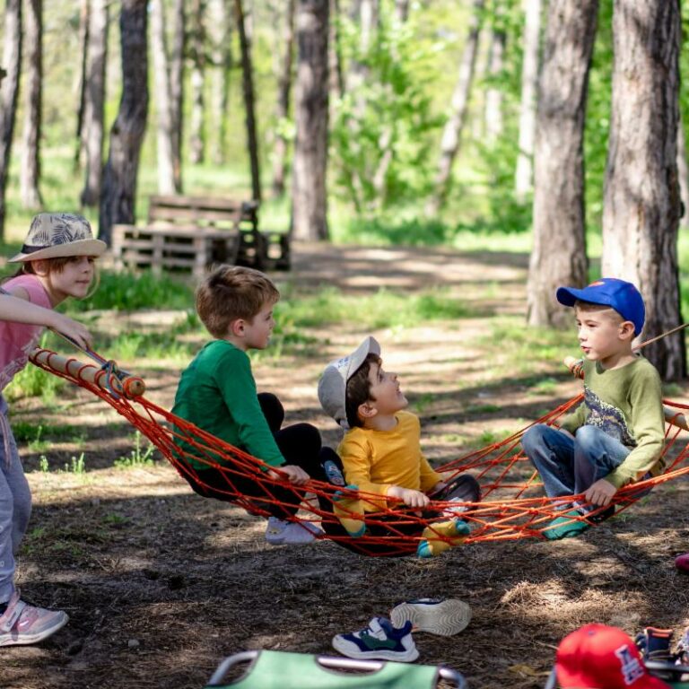 Three young children play on a hammock among trees