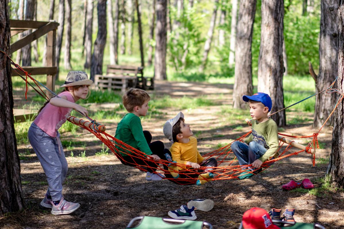 Three young children play on a hammock among trees