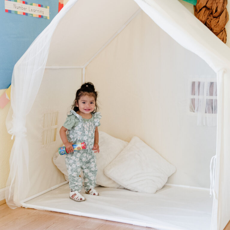 toddler stands in an indoor playhouse holding a toy