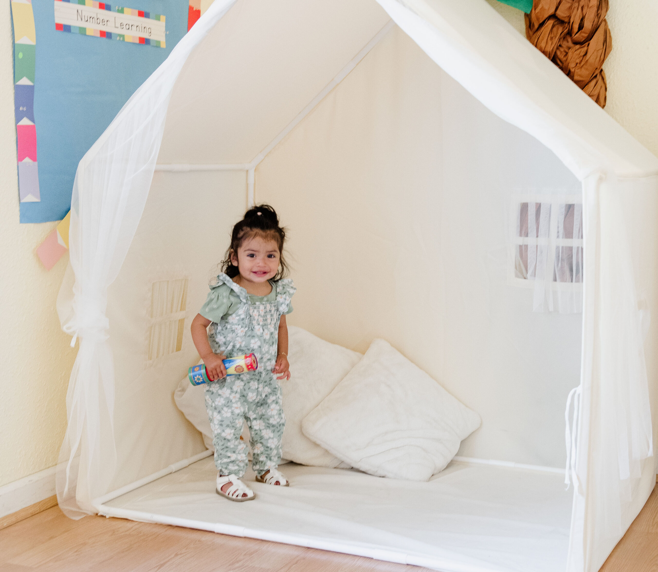 toddler stands in an indoor playhouse holding a toy