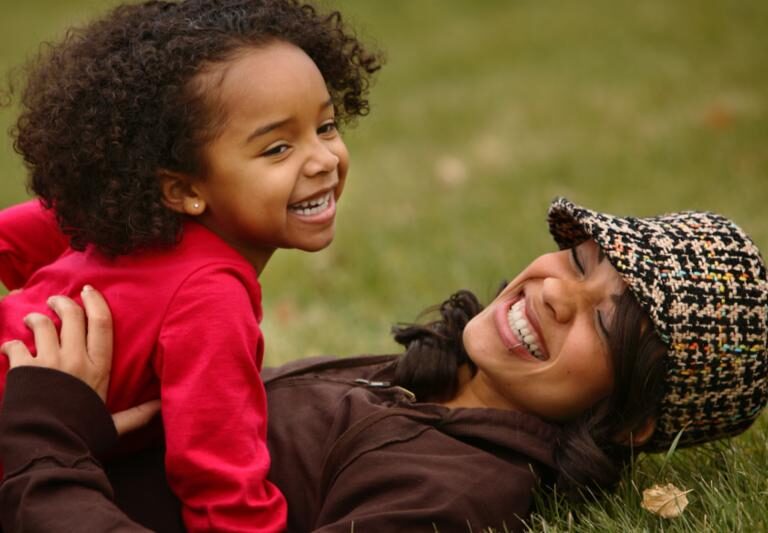 photo of mother and child laughing while laying on a field of grass