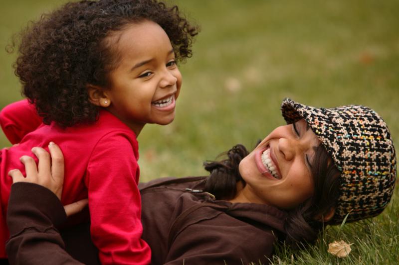 photo of mother and child laughing while laying on a field of grass